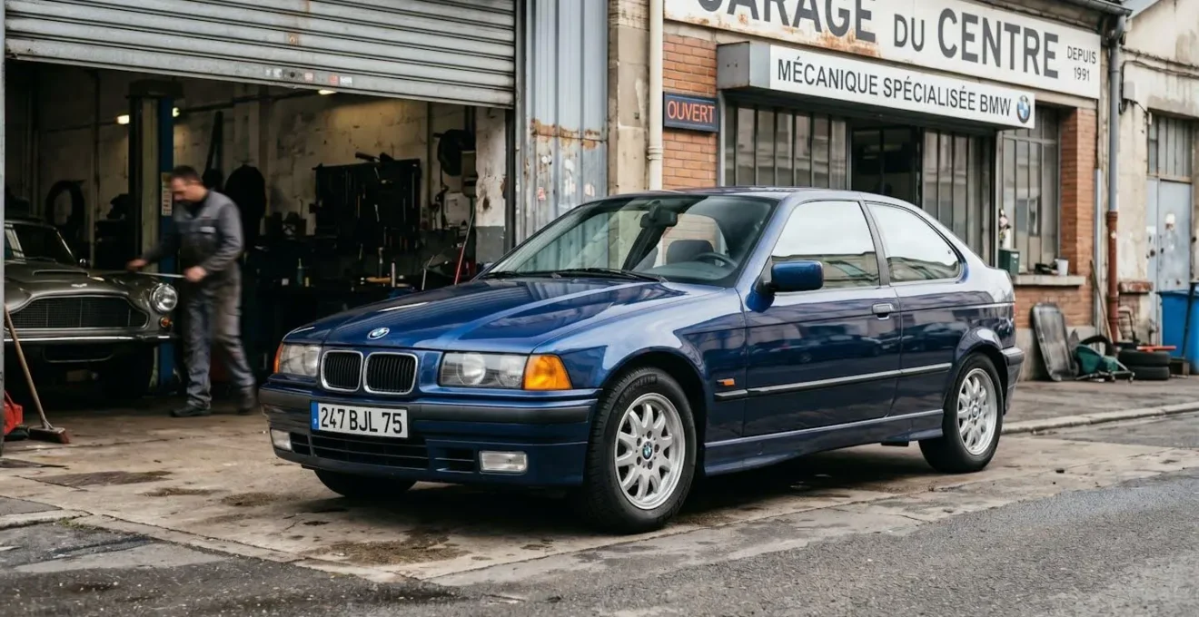 BMW Série 3 E36 en excellent état garée devant un garage spécialisé, vue 3/4 avant mettant en valeur la carrosserie soignée et les jantes d'origine.